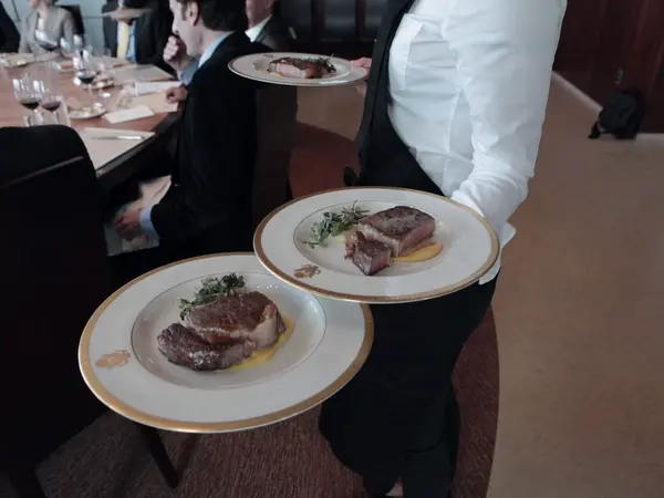 Servicekraft trägt zwei Teller mit Steak durch das Restaurant