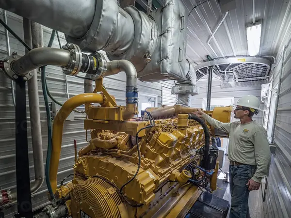 Techniker mit Schutzhelm an einem großen Motor in der Werkshalle
